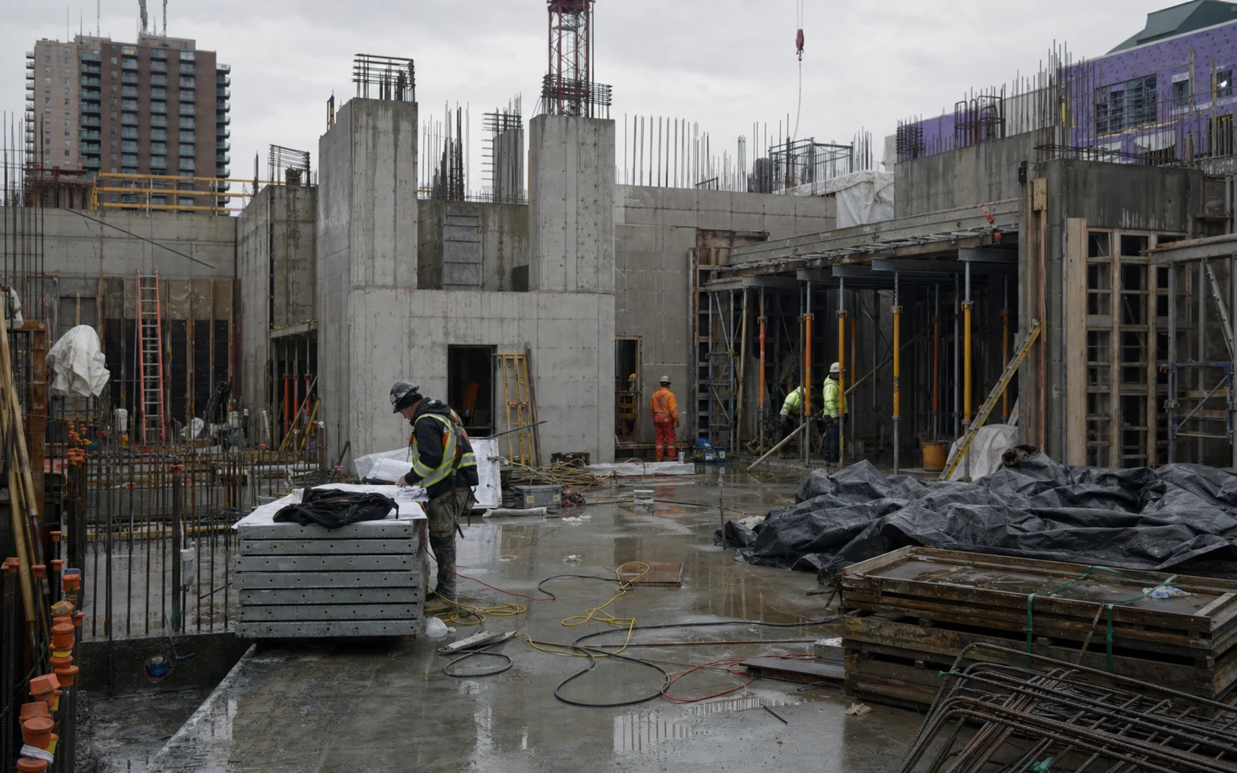 A conventional concrete and steel construction site with formwork, rebar, scaffolding, tarps, and weather-exposed materials.